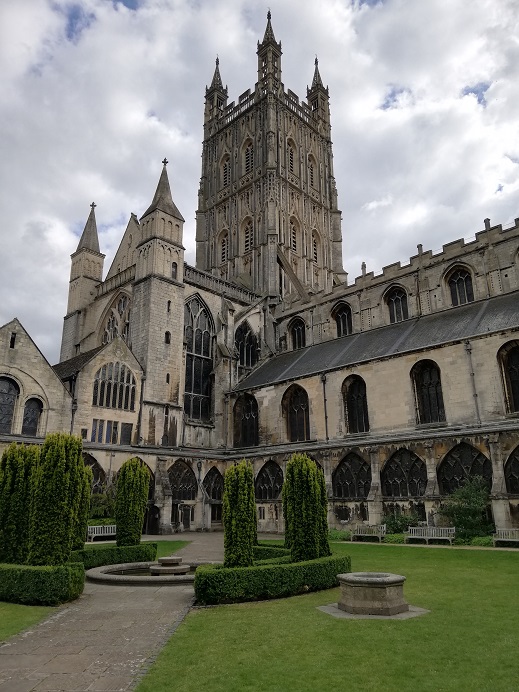 View of the bell tower from the cloisters garden, Gloucester Cathedral, with little shrubs and wells in the garden, and large windows of the cathedral visible