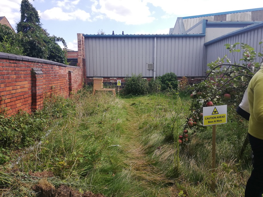A yellow sign stating bees at work warns of the beehive at the very back of the garden, away from the members of the public