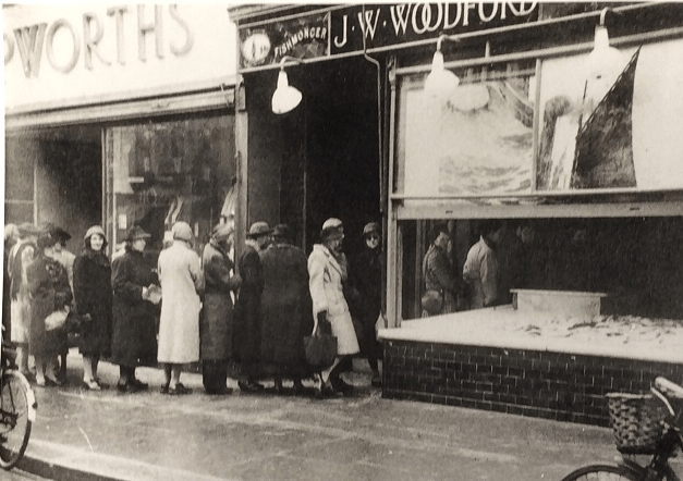 A black and white image showing a line of woman queuing to collect rationed fish supplies
