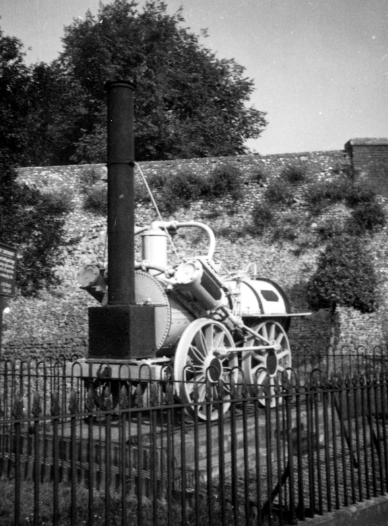 An early locomotive on display behind railings.