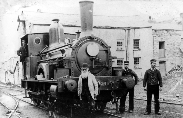Three railway employees stand in front of a huge steam engine.
