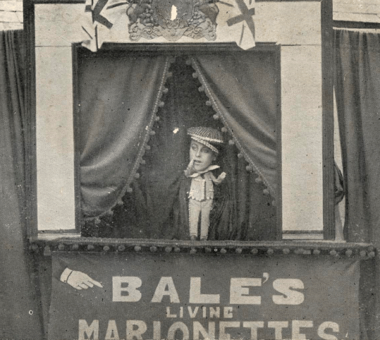 Someone performs as a puppet in a miniature theatre for a seaside show.