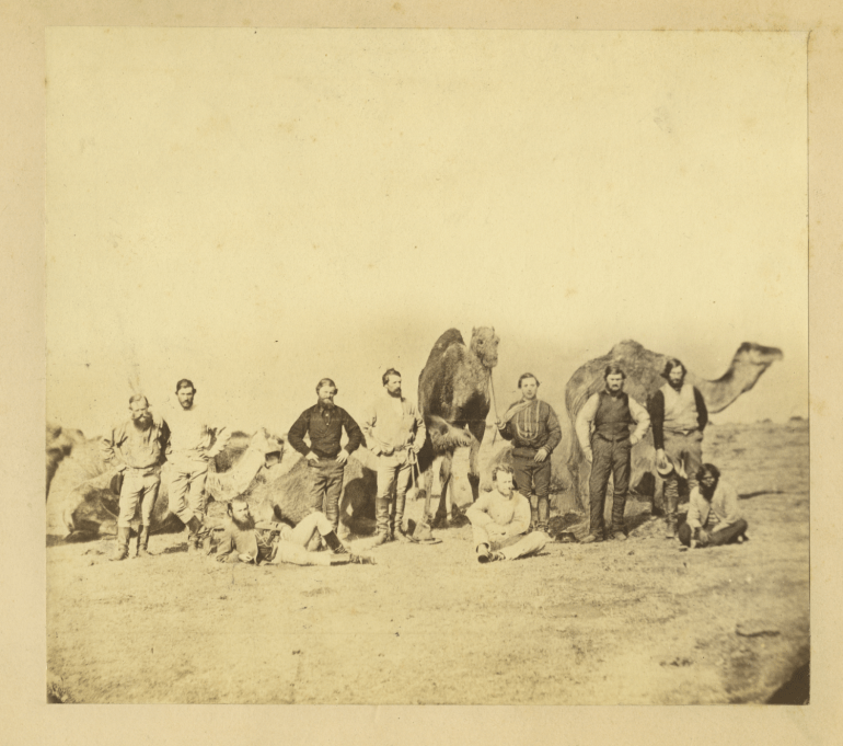 Nine male European explorers and their male Aboriginal guide gathered in the Australian outback