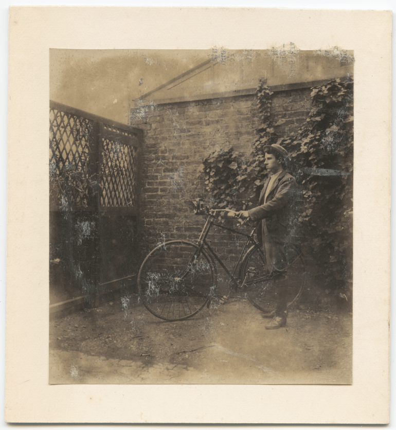 Side view of Corfield standing next to his bicycle in a backyard