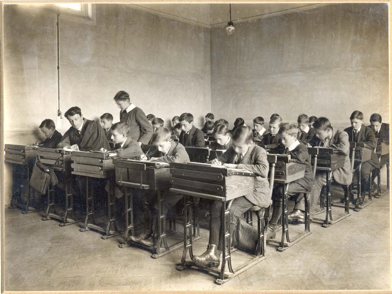 Rows of pupils sit at their desks in a schoolroom