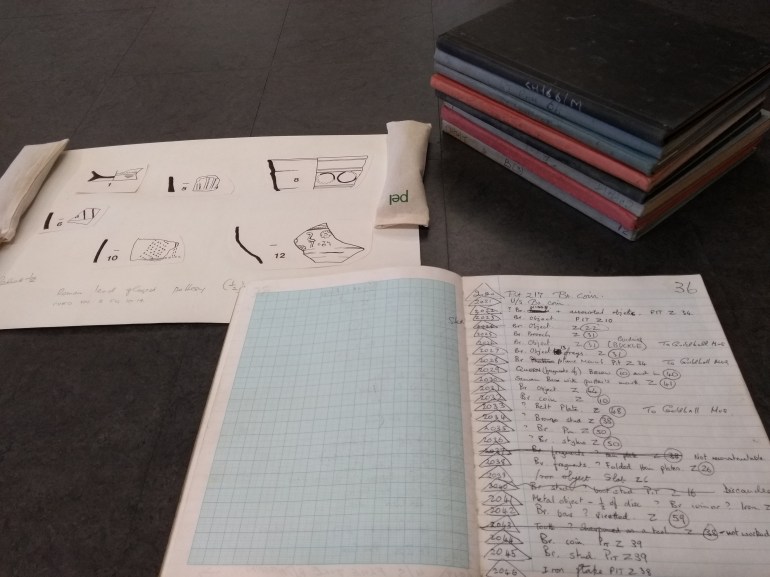 8 volumes piled on a desk. An open notebook with notes