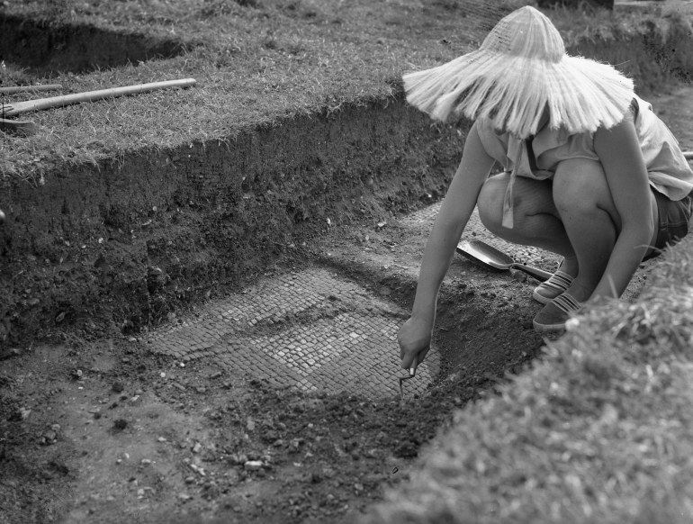 Archaeologist working at uncovering roman tiling underneath layers of dirt.