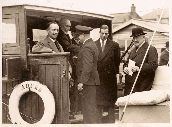 Prince George standing amongst five other men on a boat at the harbour