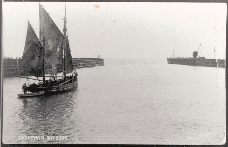 A wooden boat with sails is in the water, leaving the harbour