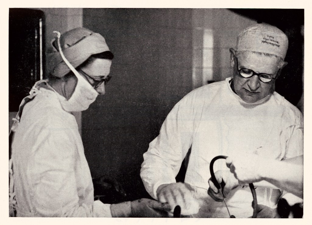 McIndoe and two nurses (one of which only has their arms in the image), working in an operating theatre
