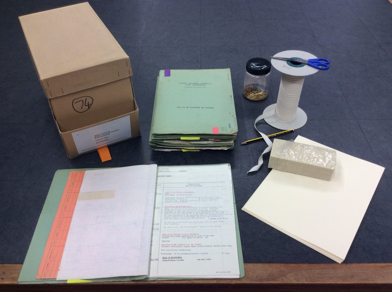 Image of the cataloguing of the collection in progress, with archival tape, scissors, a cleaning sponge, acide free card, brass paperclips and an archival box