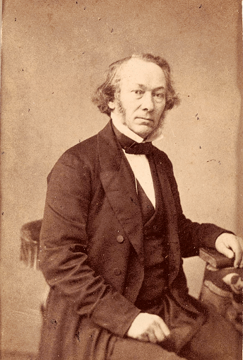 His left hand rest on a book on a side table.