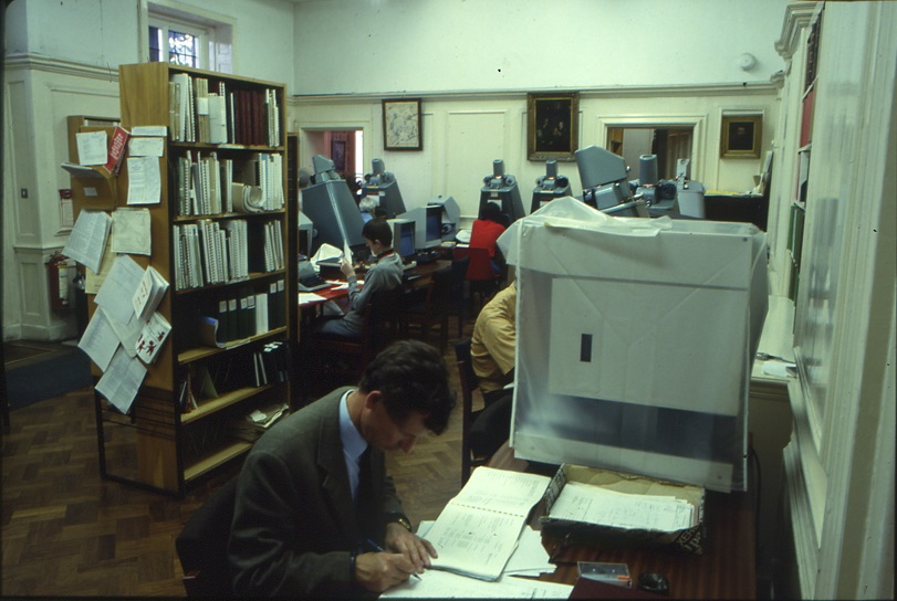 Shelving unit in middle of the room, with researchers at other microfilm readers