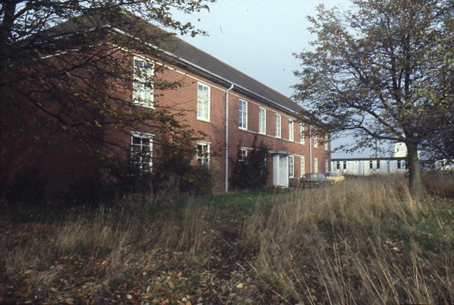 Cars by the entrance, surrounded by trees and other blocks in the background