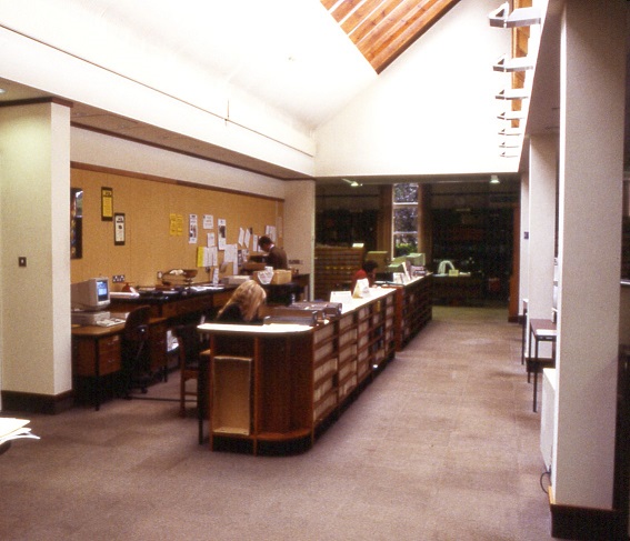 Colour photograph. Staff working at long run of desks.