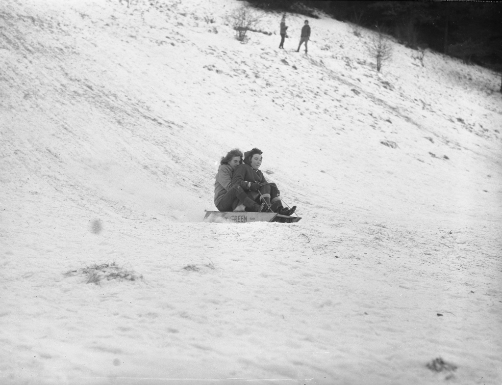 Two young women sledding down a hill in the snow.