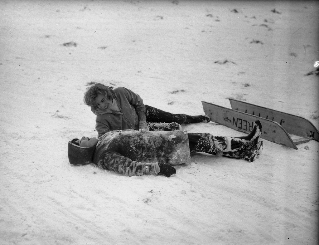 Mother and young son lying in the snow after appearing to fall off their sled.