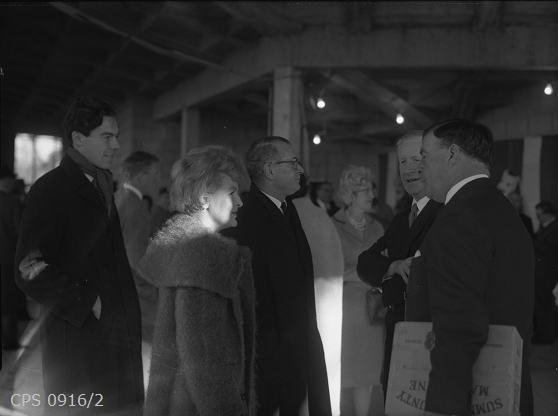 A black and white photograph of a group of well-dressed visitors to the roof topping ceremony at the Chichester Festival Theatre.