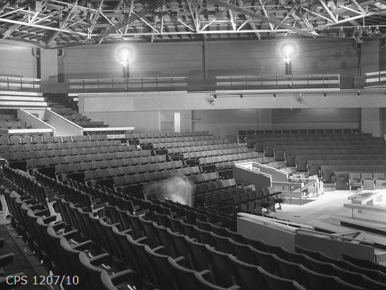 A black and white photograph of the inside of the Main House showing rows of seats and the lighting.