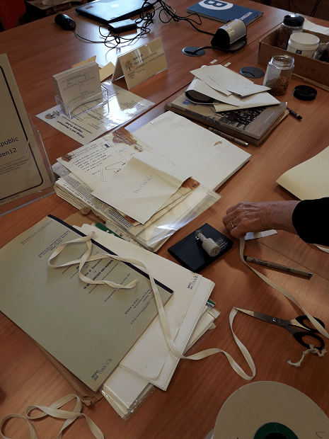 Piles of paper records, archival tape, scissors, stamps and other pieces needed to repackage items.