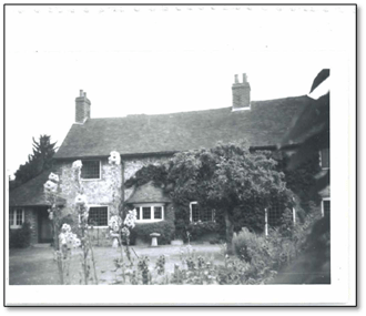 Black and white photo of a cottage covered in plants and flowers.