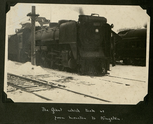 A large and imposing black old fashioned train sitting on snow covered tracks.