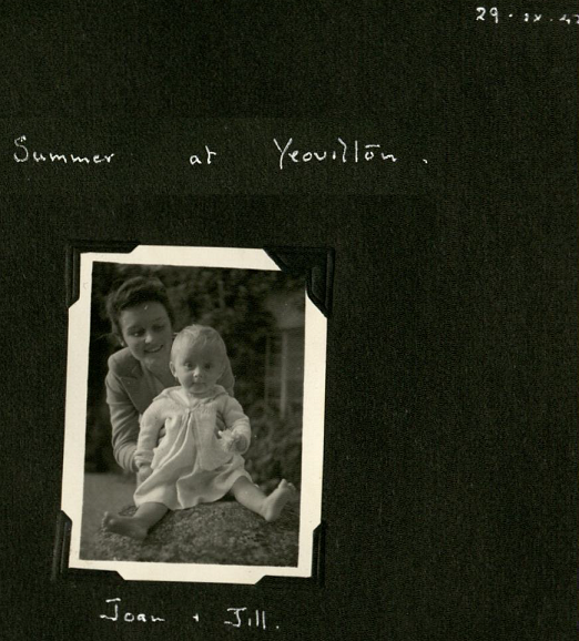 Black and white photography of a young woman holds a baby on a garden wall outside, smiling.