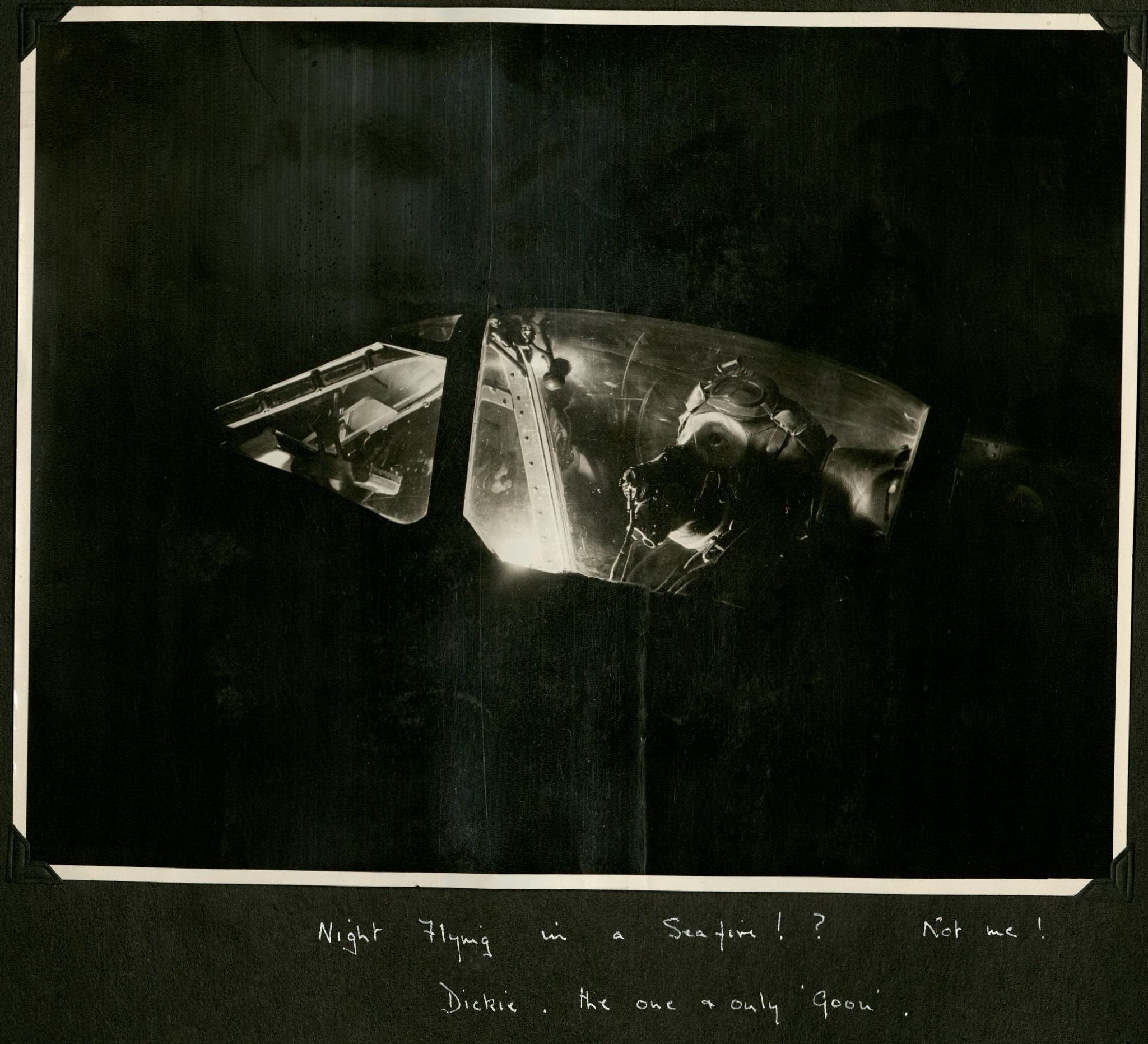 Black and white photograph of a pilot in a lit up cockpit during night-time. Caption: 'Night Flying in a Seafire!? Not me! Dickie. The one and only Goon.' On the back: 'Illustrated Copyright Photograph' [Illustrated London News].