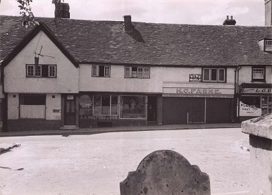 Black and white photograph. Long white wash building with tiled roof with two store fronts.