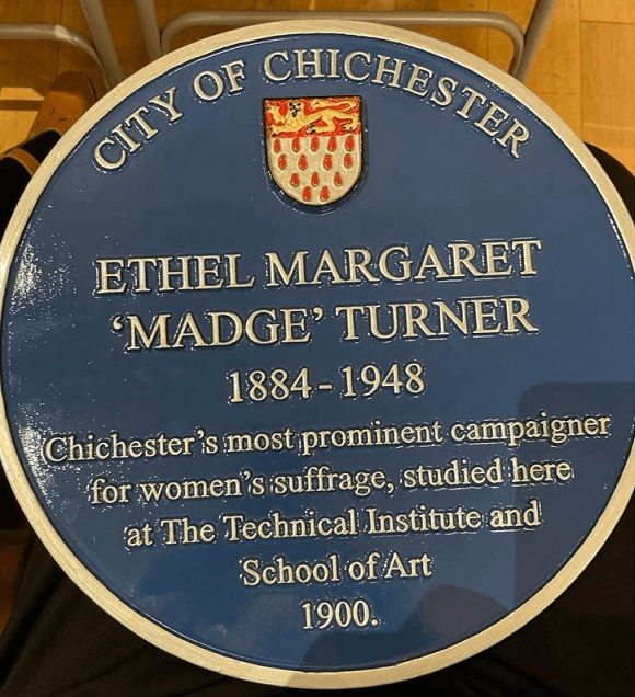 Blue circular plaque. Reads City of Chichester; followed by the coat of arms of the city; Ethel Margaret 'Madge' Turner, 1884-1948. Chichester's most prominent campaigner for women's suffrage, studied here at the Technical Institute and School of Art, 1900.