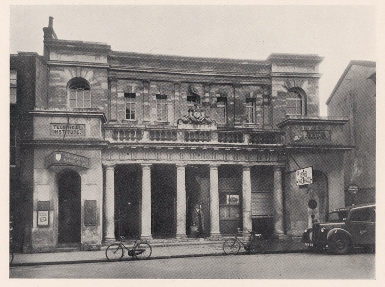 The front of the Butter Market with bicycles and a car outside, shows signs for the Chichester School of Art and the Technical Institute on the building