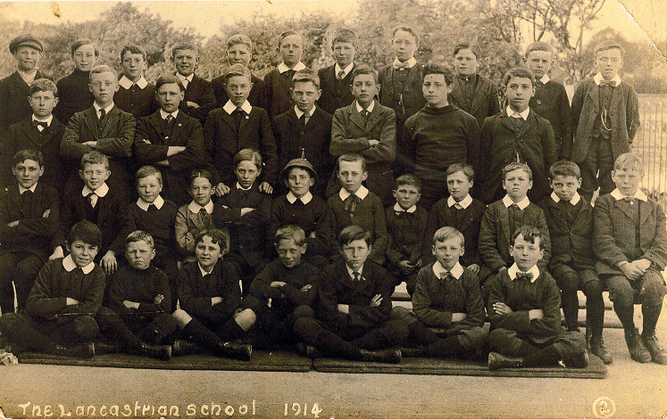 Black and white school photograph. Four rows of boys, front row sitting cross legged on the floor, second row sitting on a bench, third row standing, and fourth row standing on a bench.