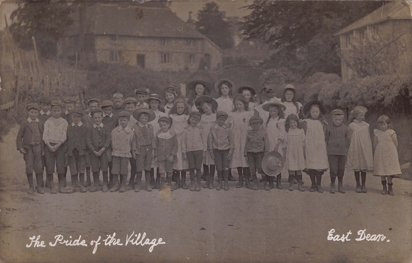 Sepia toned black and white photograph of the children of East Dean village standing in three rows depending on their age and height.