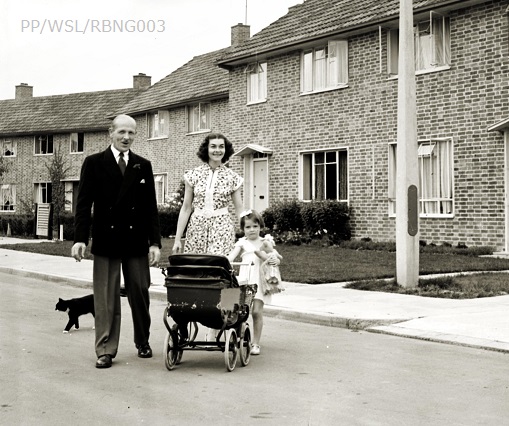 Black and white photograph of a husband and wife with their little girl who is pushing a pram; she is holding a doll. The family are standing on the road outside their new home in West Green in Crawley.